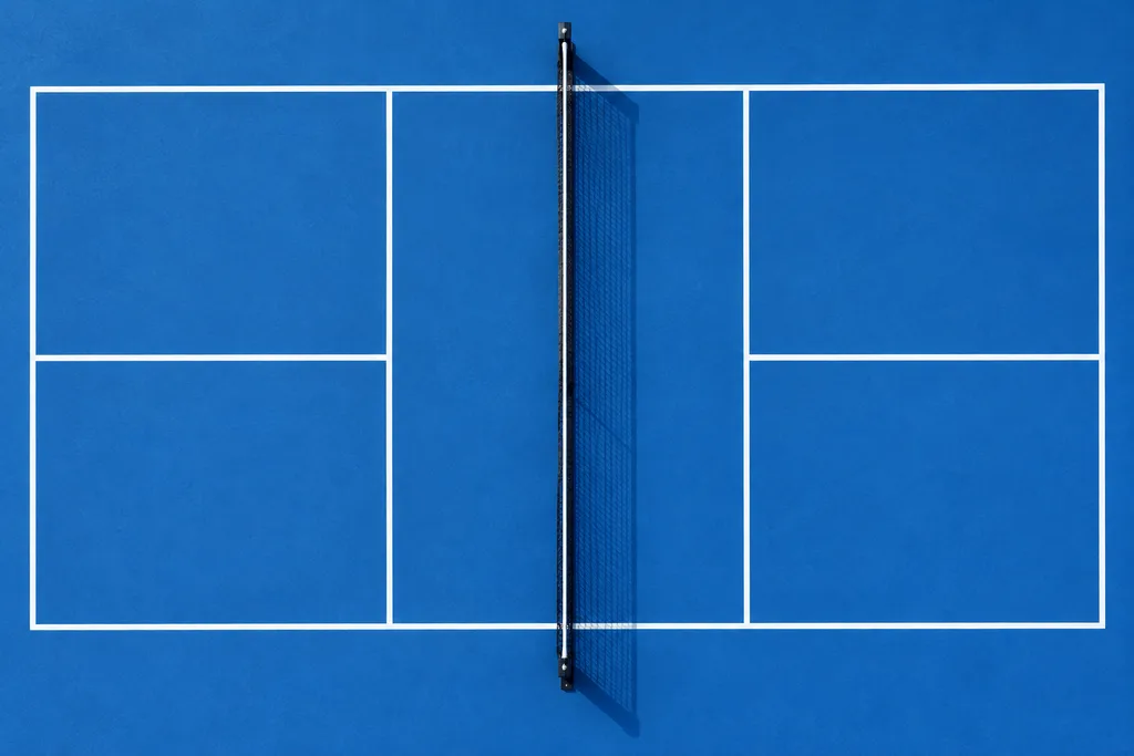Vue de dessus d'un court de pickleball dessiné au sol, avec ses lignes blanches et le filet central.